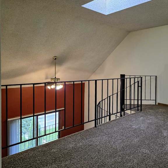 Thumbnail 9 of 11 A loft area with a black metal railing, a spiral staircase down to the living room below, and a sky light.