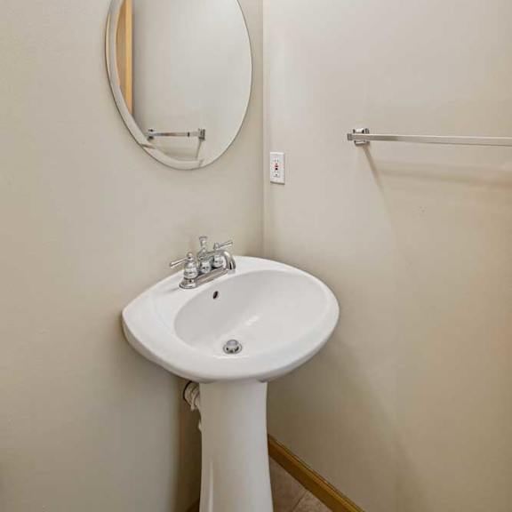 Thumbnail 35 of 54 A white pedestal sink under a round mirror with lights above it.