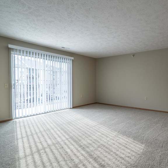 Thumbnail 17 of 22 A living room with a carpeted floor and a sliding glass door with vertical blinds