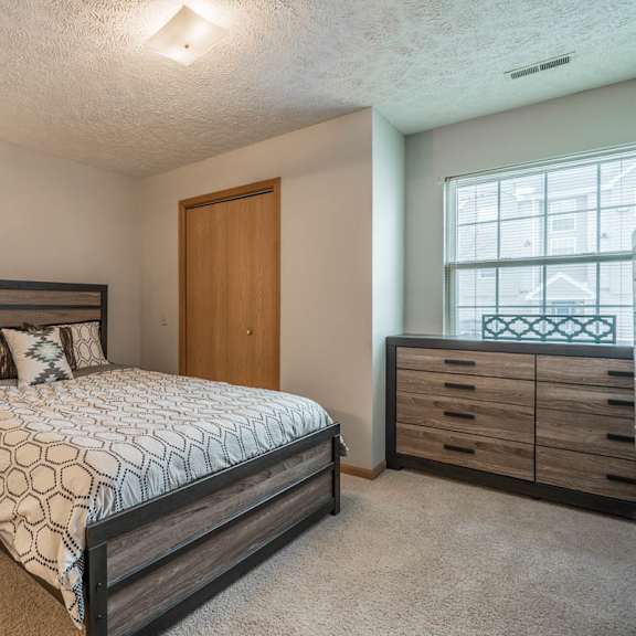 Thumbnail 9 of 13 A bedroom with a large bed, a nightstand with a lamp, and a nook with a large window
