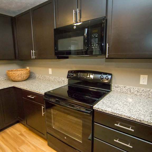 Thumbnail 6 of 13 A kitchen with dark brown cabinets, granite countertop, and black microwave and stove