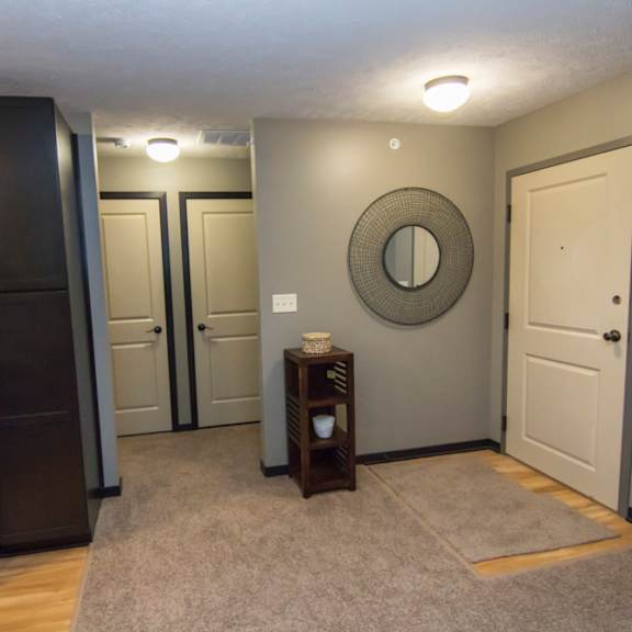 Thumbnail 9 of 13 A black refrigerator stands in a kitchen with a grey wall and a round mirror on the wall.