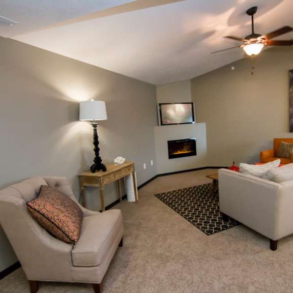 Thumbnail 8 of 13 A living room with a beige couch, a chair, a lamp, a fireplace, and a fireplace