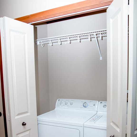 Thumbnail 13 of 14 A white washer and dryer in a small laundry closet with storage shelf above it