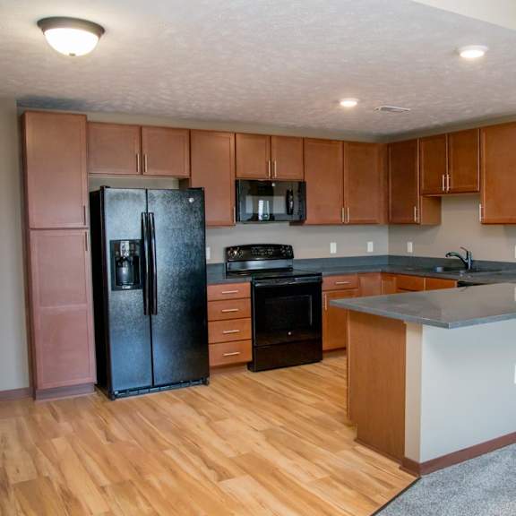 Thumbnail 4 of 15 A kitchen with wooden floors and a black refrigerator.