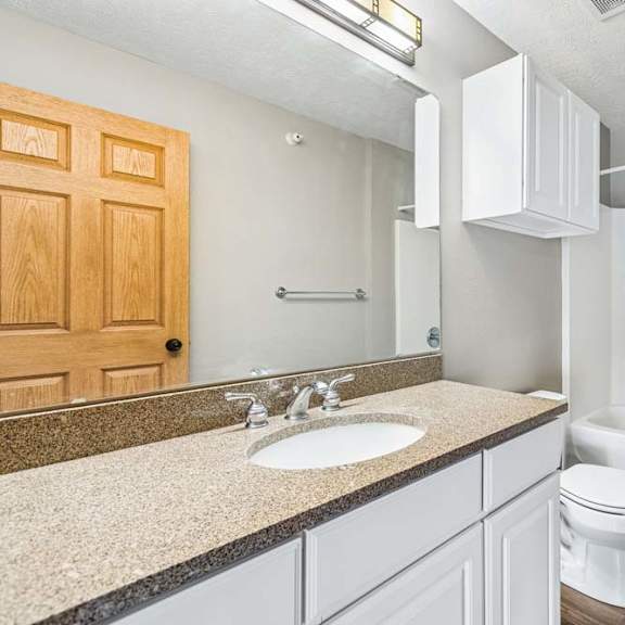 Thumbnail 27 of 31 Apartment bathroom featuring white cabinetry, large mirror, and bathtub.