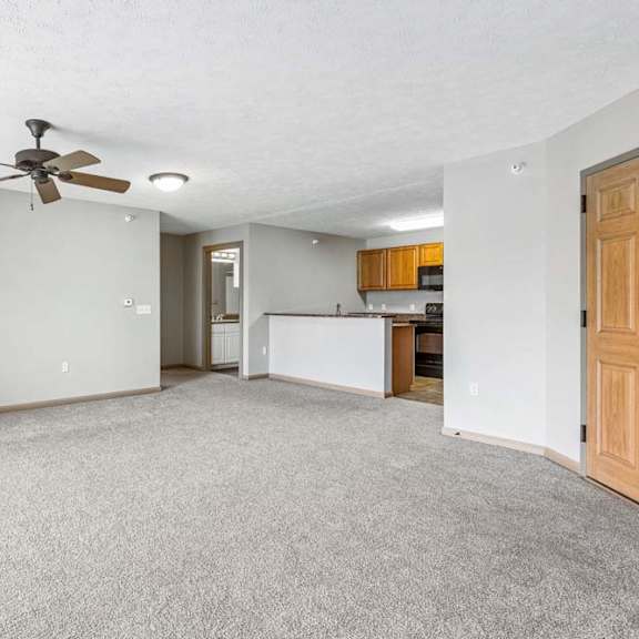 Thumbnail 18 of 31 Carpeted living space with ceiling fan and adjacent kitchen.