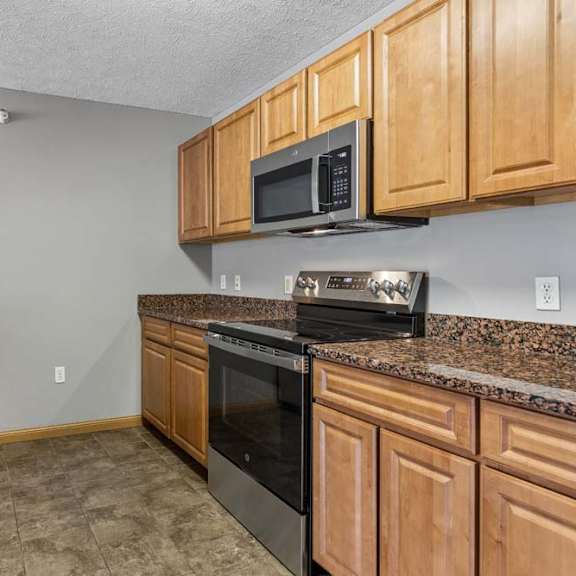 Thumbnail 4 of 19 Modern kitchen featuring granite counters, wood cabinets, and stainless steel appliances.