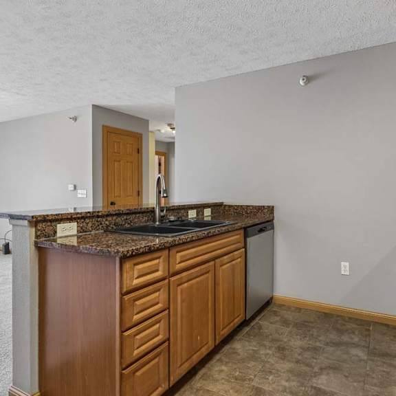 Thumbnail 5 of 19 Open kitchen with granite peninsula counter, wood cabinetry, and tile flooring.