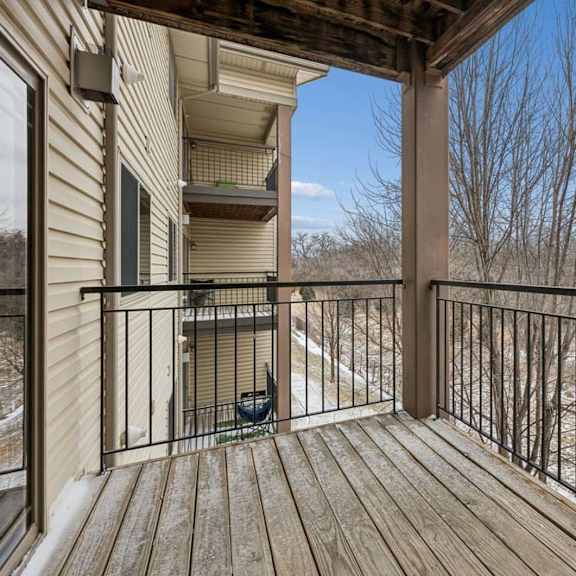Thumbnail 26 of 26 Private apartment balcony with wood decking, metal railing, and views of mature trees, offering an outdoor space accessible from the apartment.