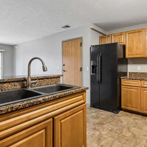 Thumbnail 15 of 26 Apartment kitchen with wood cabinets, black appliances, laminate countertops, and a center island with a sink, offering an open layout to the living area.