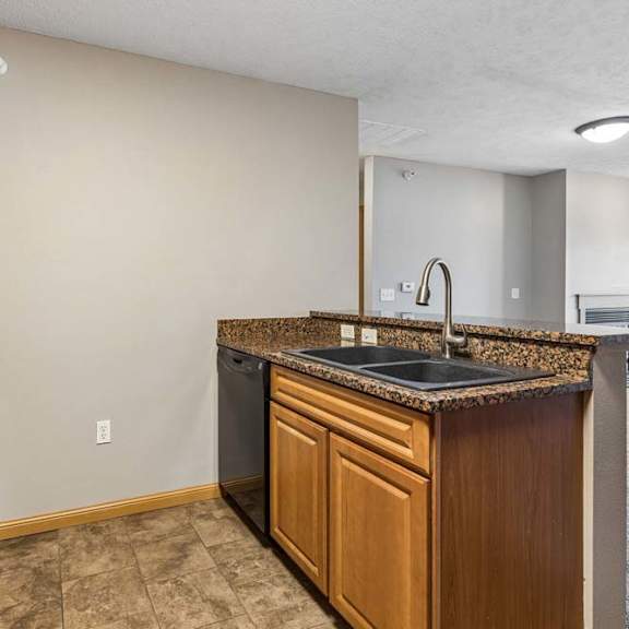Thumbnail 13 of 26 Open apartment kitchen with wood cabinets, laminate countertops, a breakfast bar, black appliances, and a sink overlooking the adjacent living area.