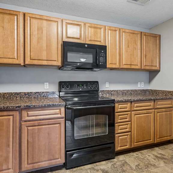 Thumbnail 14 of 26 Apartment kitchen with wood cabinets, laminate countertops, black oven and microwave, and ample upper and lower cabinet storage.
