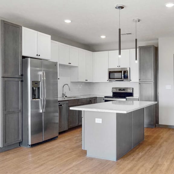 Thumbnail 14 of 19 Slate finish kitchen with two tone cabinets, light hard wood style flooring, granite counter tops, and white back splashes in the Bliss floor plan at Haven at Uptown in Lincoln, NE