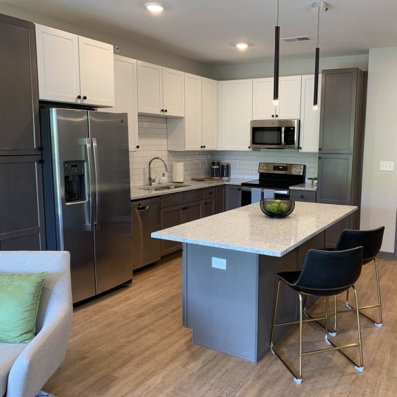 Thumbnail 2 of 19 Furnished kitchen in the Slate finish with two tone cabinets, hard wood style flooring, and granite counter tops in the Bliss floor plan at Haven at Uptown