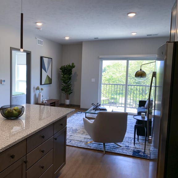 Thumbnail 4 of 19 Large kitchen island and furnished living room looking out onto scenic view in Bliss floor plan at Haven at Uptown.