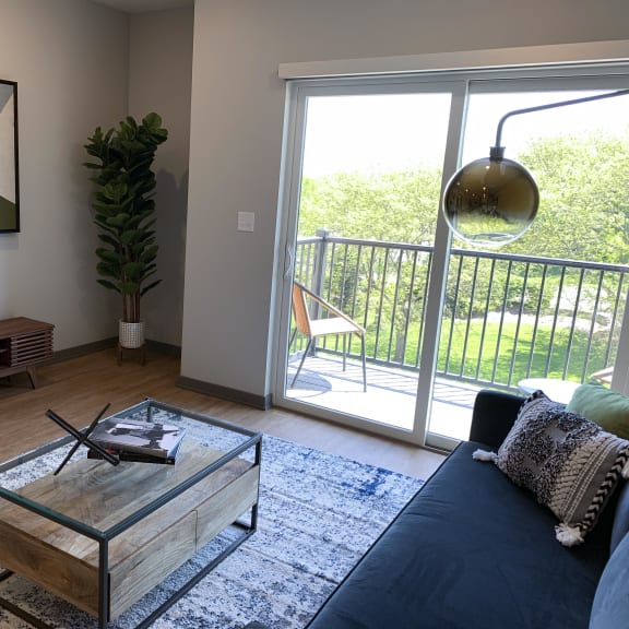 Thumbnail 5 of 19 Spacious furnished living room with hard wood style flooring and scenic view of tree line in Lincoln at Haven at Uptown.