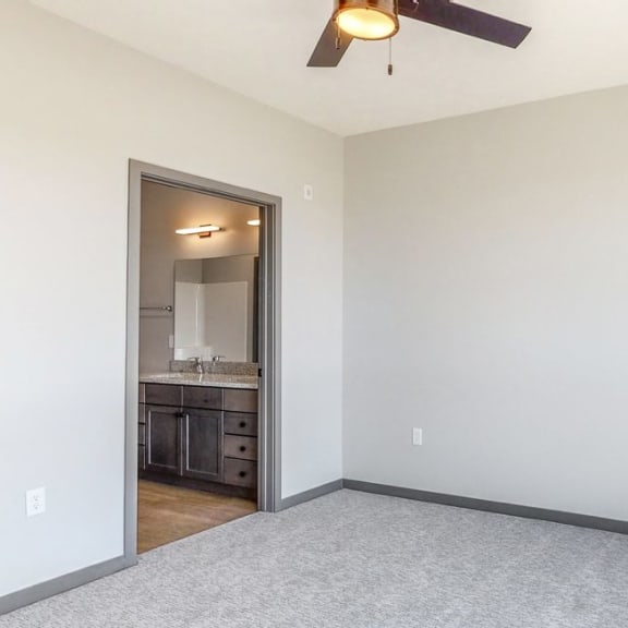 Thumbnail 14 of 18 Master bedroom with large windows providing natural light, ceiling fan, and attached bathroom at Haven at Uptown in Lincoln, NE