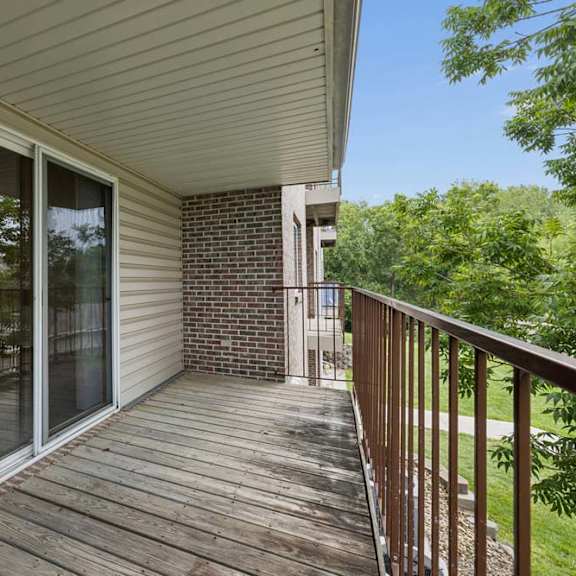 Thumbnail 37 of 37 Covered private balcony with wood decking, a sliding glass door, metal railing, and leafy green views.