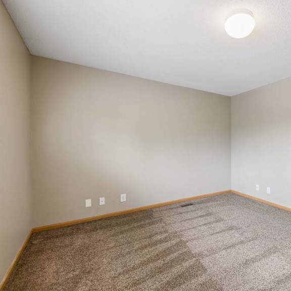 Thumbnail 21 of 26 Empty apartment bedroom with neutral carpet, beige walls, wood trim, and an open doorway leading to the adjoining hallway.