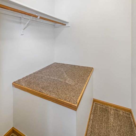Thumbnail 22 of 26 Walk-in apartment closet with a hanging rod, upper shelf, neutral walls, and a built-in storage ledge for added organization.
