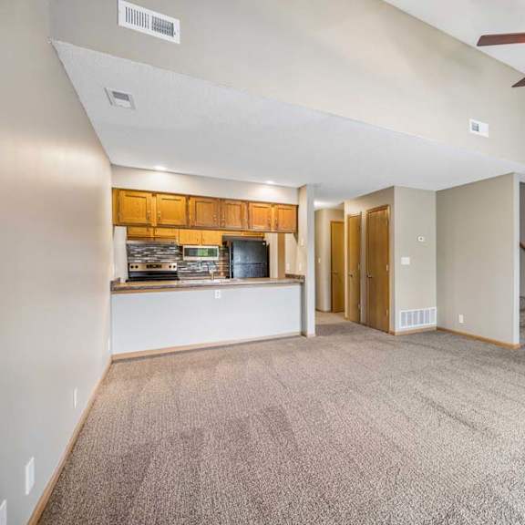 Thumbnail 16 of 26 Bright, open-concept apartment living room with neutral carpet, a ceiling fan, breakfast bar overlooking the kitchen, wood-tone cabinets, and a staircase leading to the upper level.