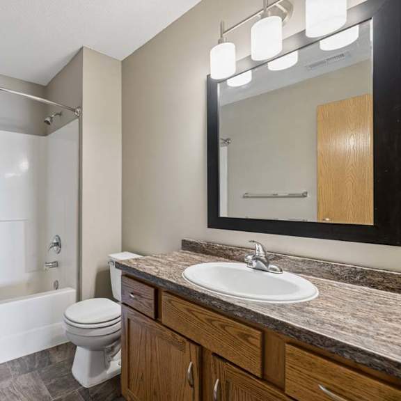 Thumbnail 20 of 21 Full bathroom with a tub-shower combination, wood vanity, stone-look countertop, framed mirror, and modern vanity lighting.