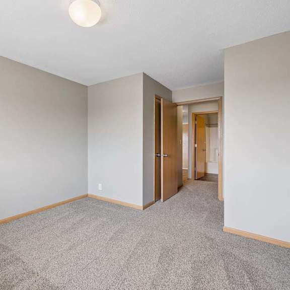 Thumbnail 17 of 21 Unfurnished bedroom with soft carpeting, an angled entryway, and open doors connecting to the hall and nearby bathroom.