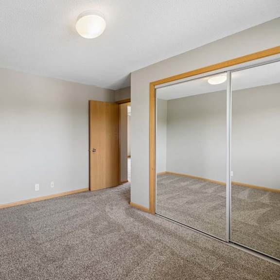 Thumbnail 15 of 21 Bedroom with wall-to-wall carpeting and large mirrored closet doors that reflect the open layout and overhead lighting.