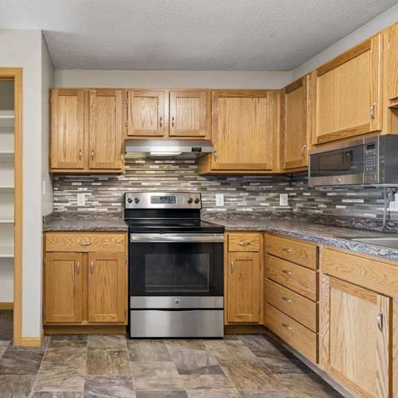 Thumbnail 12 of 21 Kitchen with oak cabinets, stone-look counters, mosaic backsplash, stainless oven and microwave, plus a tall shelved pantry.