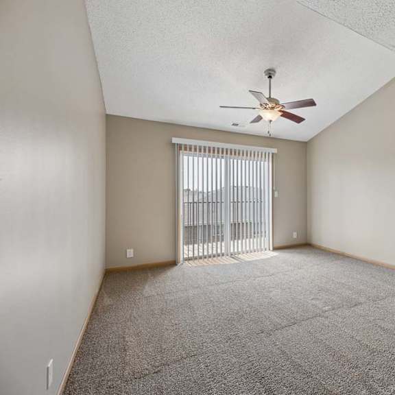 Thumbnail 13 of 21 Vaulted living room with a ceiling fan, sliding glass door to the balcony, and an open doorway to an adjoining room.