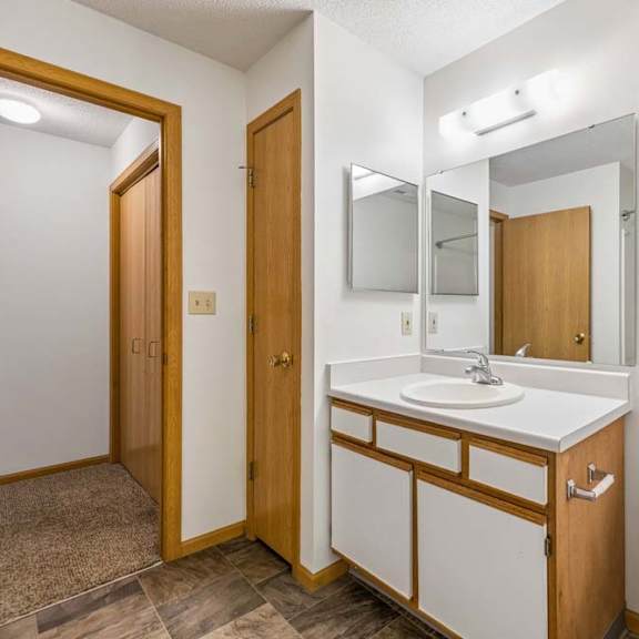 Thumbnail 28 of 31 Apartment bathroom with a single-sink vanity, large wall mirror, toilet, and neutral finishes, with the hallway and bedroom visible through the open doorway.