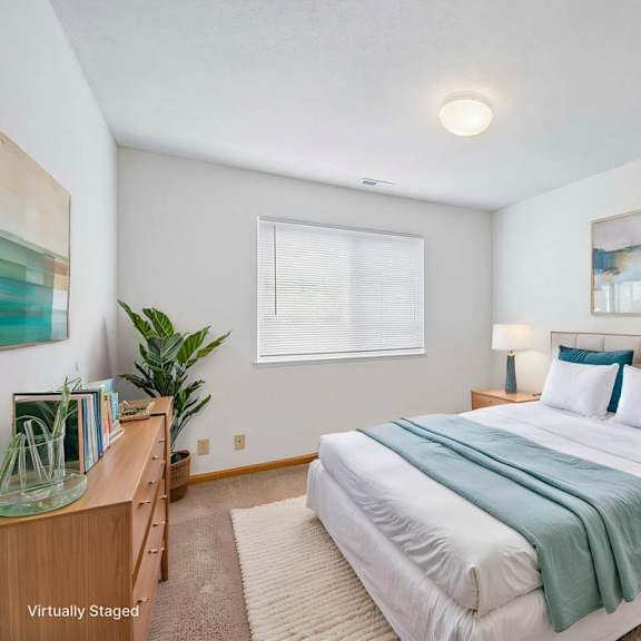 Thumbnail 3 of 16 Virtually staged bedroom with a large bed, bedside lamps, window, artwork, and wood-look flooring in a bright interior.