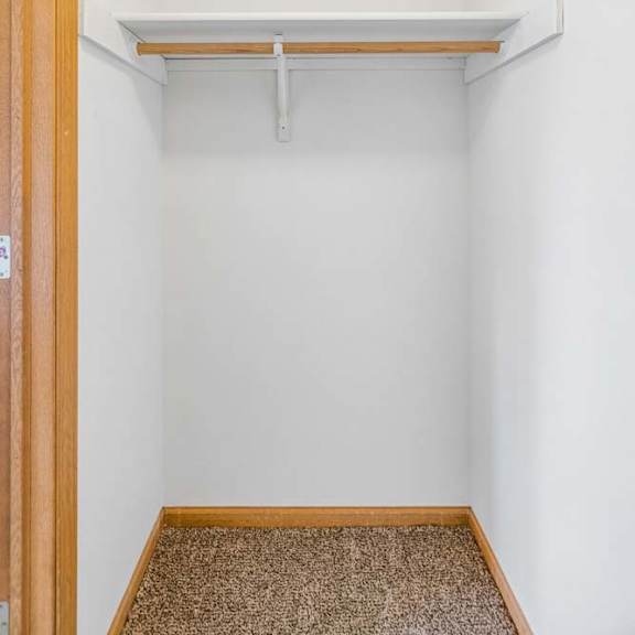 Thumbnail 26 of 31 Apartment closet with a single hanging rod, upper shelf, neutral walls, and carpeted flooring for convenient storage.