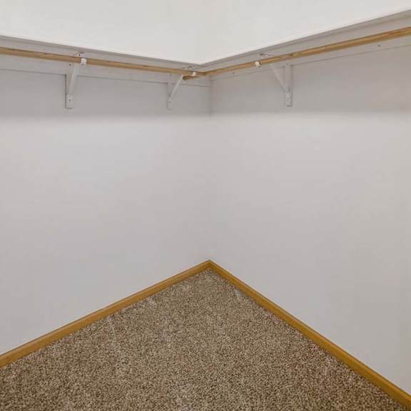 Thumbnail 23 of 31 Walk-in apartment closet with wraparound hanging rods, upper shelving, neutral walls, and carpeted flooring for organized storage.
