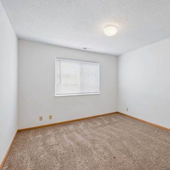 Thumbnail 22 of 31 Bright, empty apartment bedroom with neutral carpet, white walls, wood trim, and a window with blinds that provides natural light.
