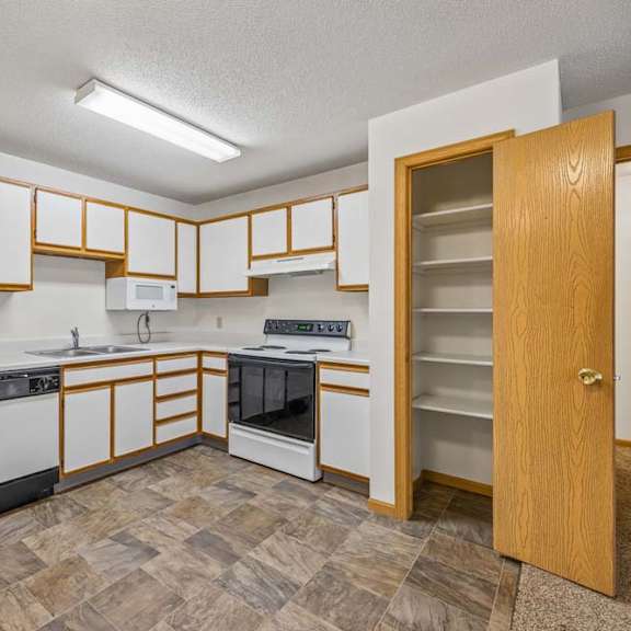 Thumbnail 17 of 31 Spacious apartment kitchen with white cabinets, white appliances, a freestanding oven, durable flooring, and a built-in pantry for additional storage.
