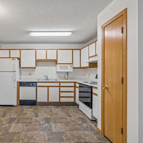 Thumbnail 18 of 31 Open apartment kitchen with white cabinets, white appliances, durable flooring, and a pass-through breakfast bar connecting to the adjacent living area.
