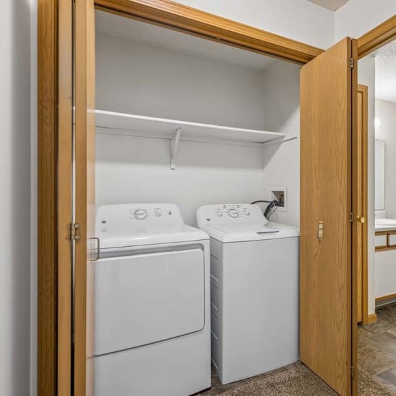 Thumbnail 29 of 31 Apartment laundry closet with a full-size washer and dryer, bi-fold wood doors, and an adjacent bathroom featuring a single-sink vanity and tub/shower combination.