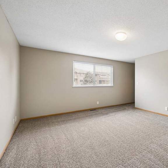 Thumbnail 12 of 18 Spacious apartment bedroom with carpeted flooring, neutral walls, a large window providing natural light, and an open doorway leading to the adjoining bathroom.