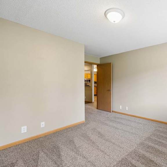 Thumbnail 10 of 18 Bright apartment bedroom with carpeted flooring, neutral walls, a window with blinds providing natural light, and an open doorway leading toward the walk-in closet.