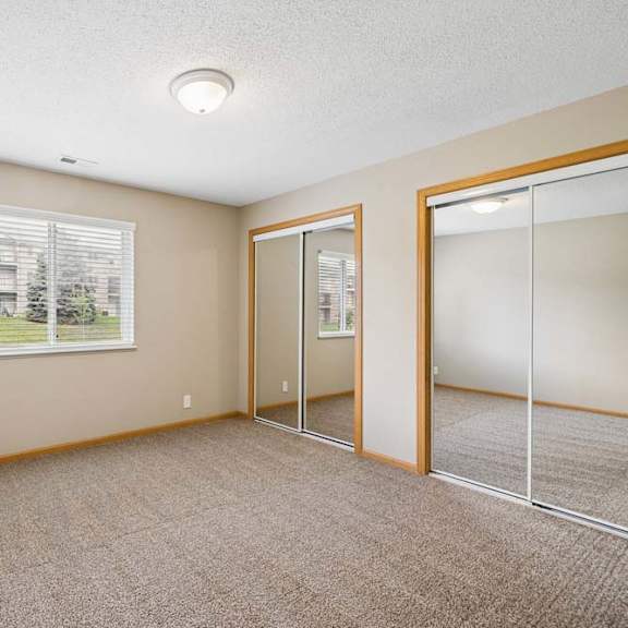 Thumbnail 11 of 18 Bright apartment bedroom with carpeted flooring, a window providing natural light, and mirrored sliding closet doors for convenient storage.