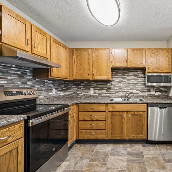 Thumbnail 5 of 18 Apartment kitchen with wood cabinetry, laminate countertops, a tile backsplash, black and stainless steel appliances, and a functional U-shaped layout adjacent to the living area.