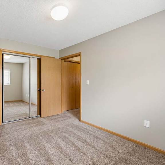 Thumbnail 22 of 28 Bright apartment bedroom with carpeted flooring, neutral walls, mirrored sliding closet doors, and a separate walk-in closet for additional storage.