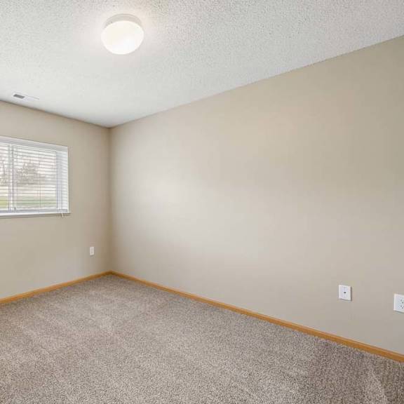 Thumbnail 23 of 28 Bright apartment bedroom with carpeted flooring, neutral walls, and a window with blinds providing natural light.