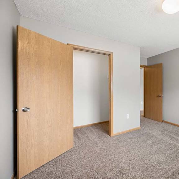 Thumbnail 21 of 28 Bright apartment bedroom with carpeted flooring, an open closet with sliding doors, neutral walls, and a separate entry door for convenient access.