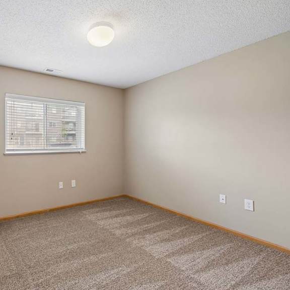 Thumbnail 24 of 28 Bright apartment bedroom with carpeted flooring, neutral walls, and a window with blinds providing natural light.