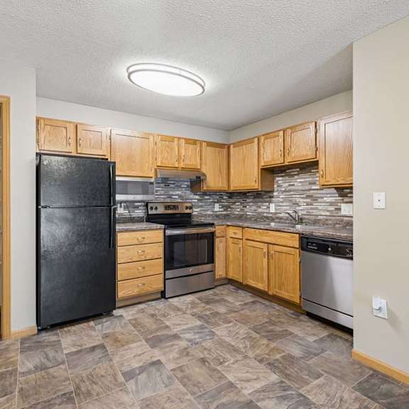 Thumbnail 16 of 28 Apartment kitchen with wood cabinetry, a tile backsplash, laminate countertops, black and stainless steel appliances, and a pantry with built-in shelving in a functional U-shaped layout.