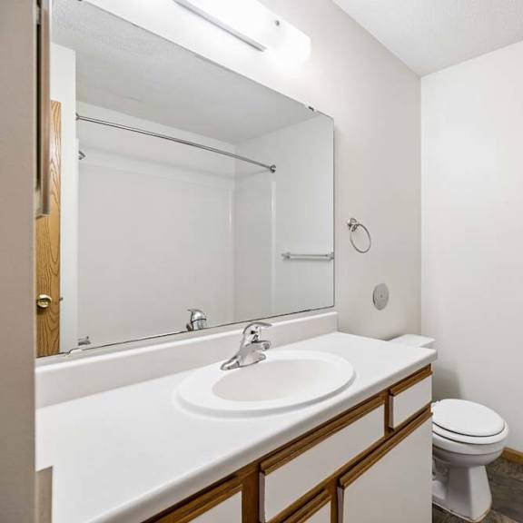 Thumbnail 22 of 23 Apartment bathroom with a single-sink vanity, white and wood-tone cabinetry, a large mirror with overhead lighting, and a tub-shower combination with a towel bar.