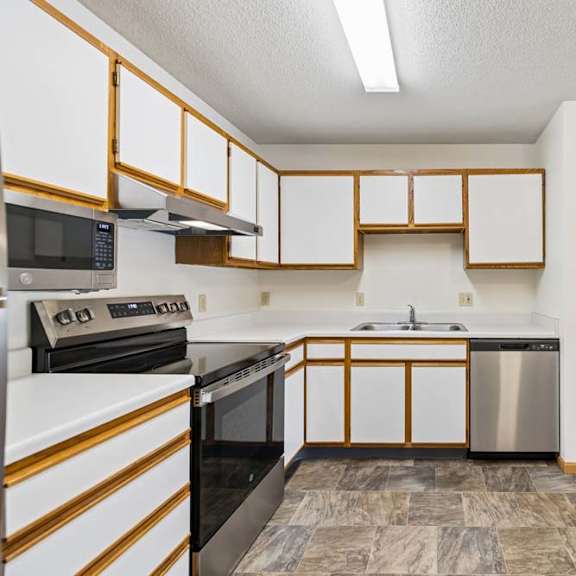 Thumbnail 10 of 23 Apartment kitchen with white and wood-tone cabinetry, laminate countertops, stainless steel dishwasher, black oven, and a functional U-shaped layout open to the adjacent living area.